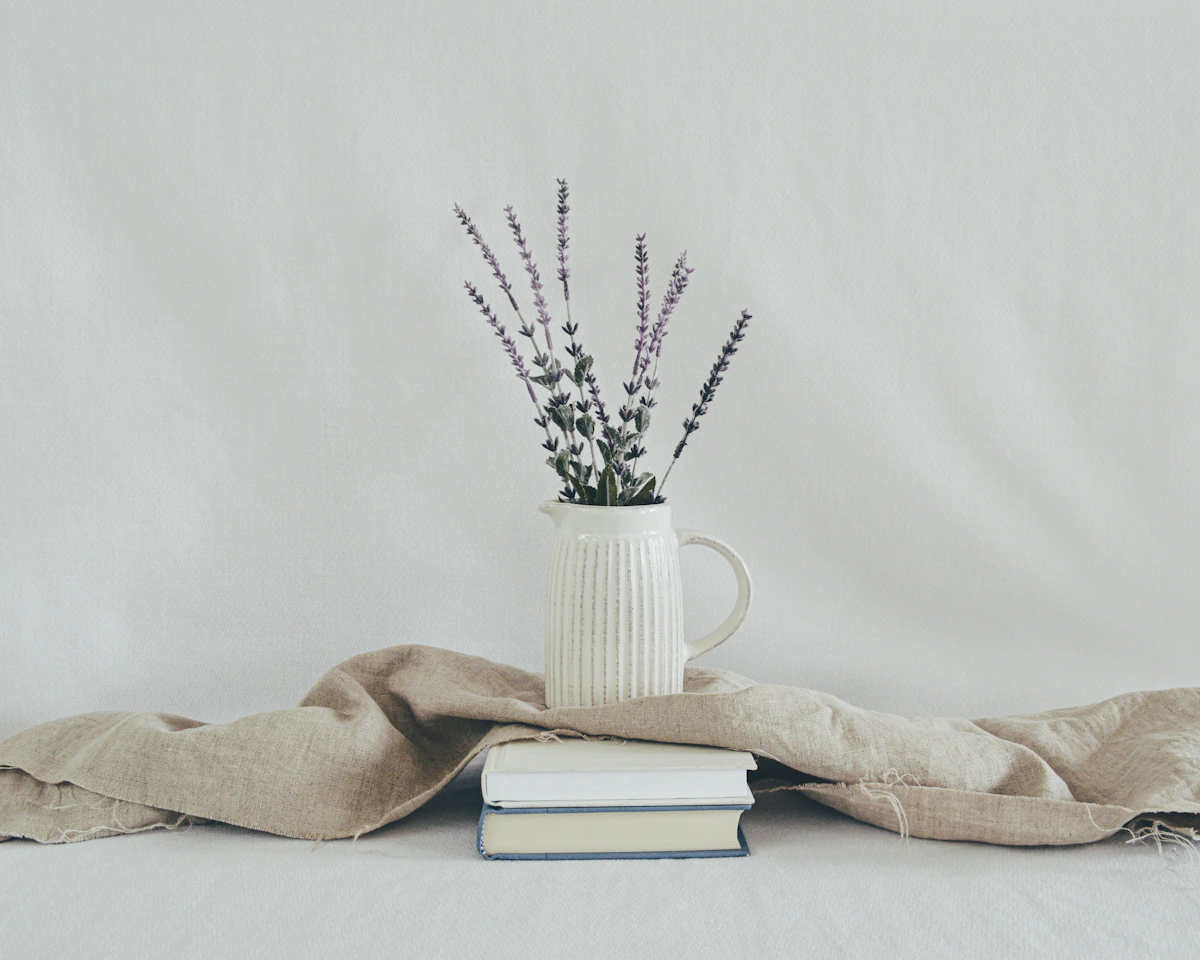 Jarra de cerámica blanca con flores sobre libros y lino